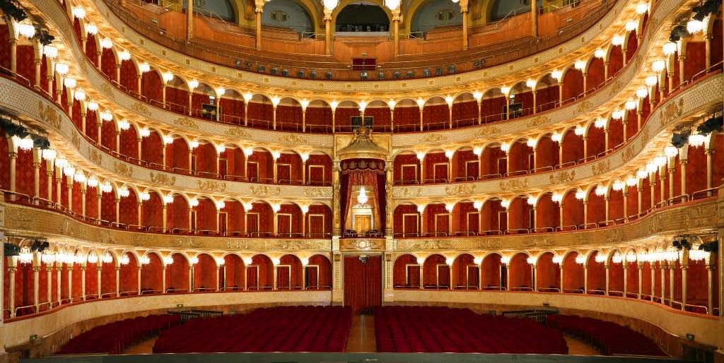 Arquitectura interior del Teatro dell’Opera di Roma: elegancia y tradición italiana Vista interior del Teatro dell’Opera di Roma, destacando las butacas rojas y el techo decorado con detalles arquitectónicos clásicos